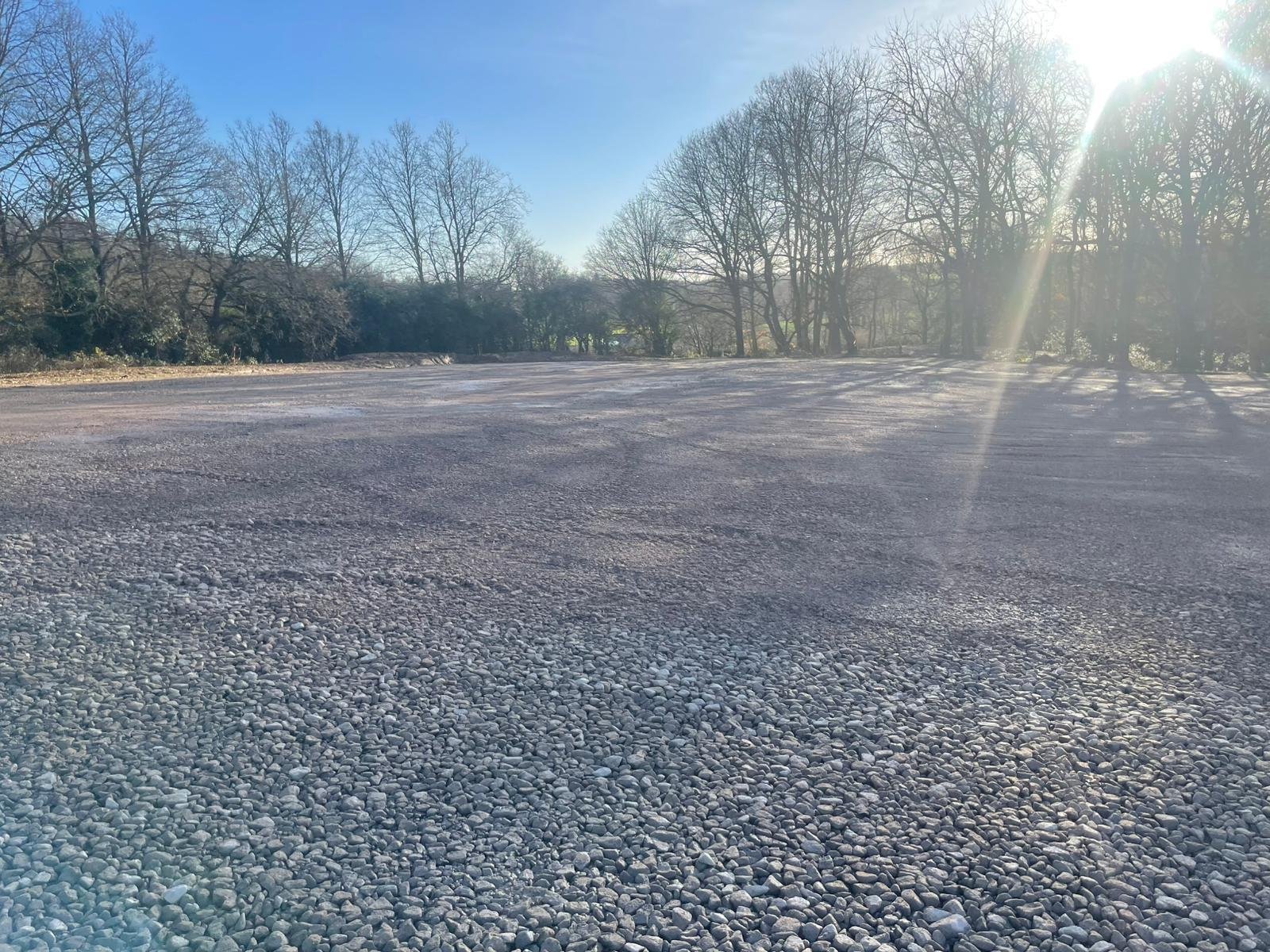 Expansive gravel surface with sunlight across a wooded backdrop